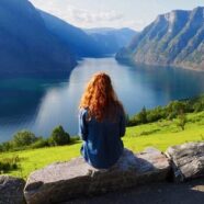 Rear View Of Woman Sitting On Rock By Lake